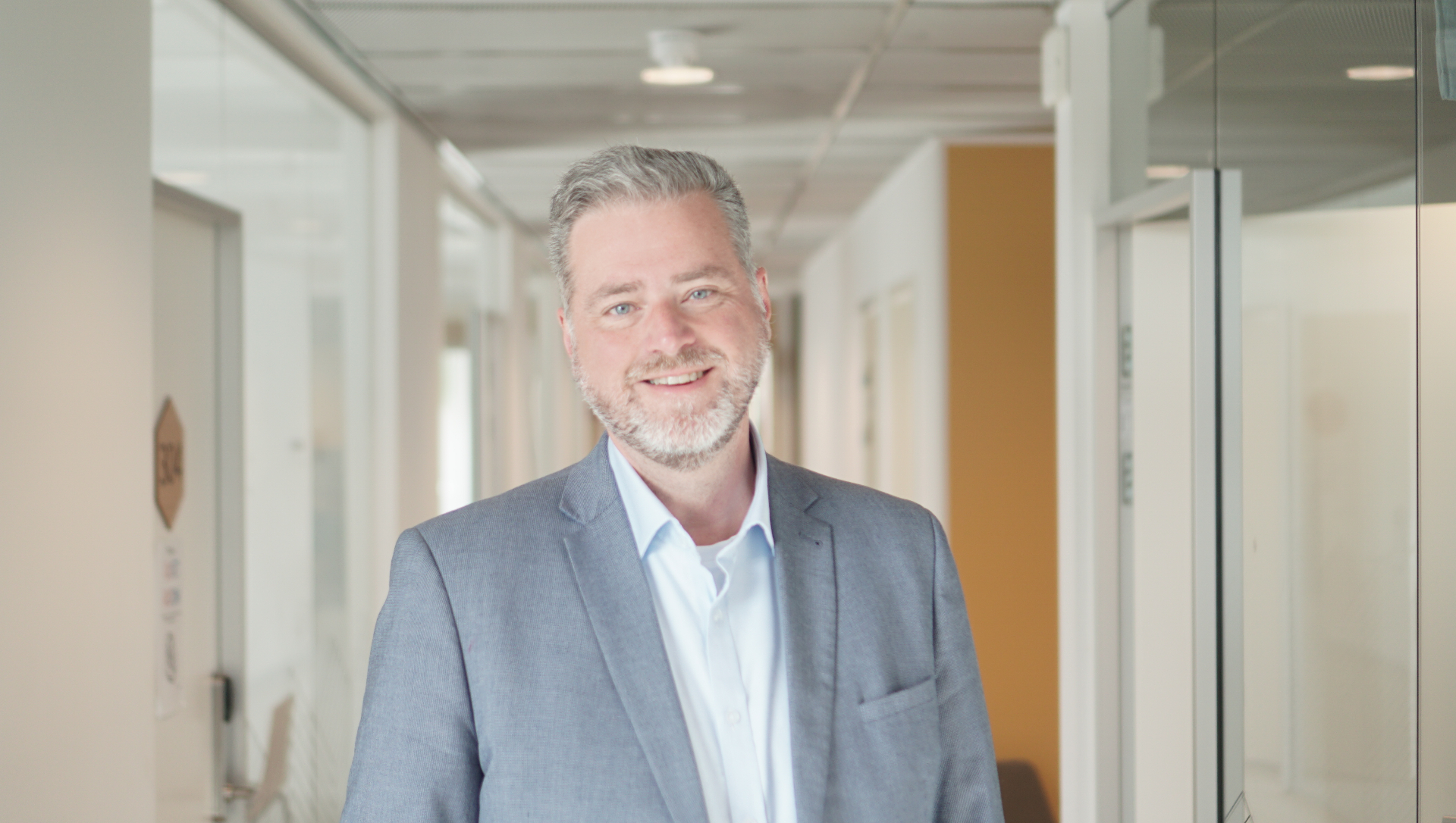Simon Wright in a light grey suit, smiling in a modern office hallway
